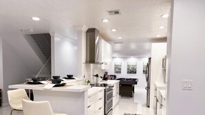 Una cocina moderna con armarios blancos, electrodomésticos de acero inoxidable y una isla central con taburetes de bar.