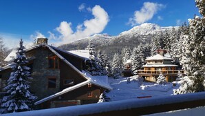 A snow-covered lodge with a stone exterior and wooden accents, surrounded by snow-laden trees and mountains.