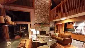 A spacious living area with a stone fireplace, a dining table with chairs, a sofa, and a kitchen area with modern appliances.