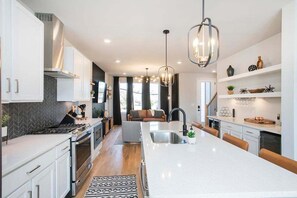 A modern kitchen with a large island, white cabinetry, and pendant lighting. - 🌇 Nashville Rooftop Retreat - Fire Pit, Skyline Views, Sleeps 12! 🎶 (Nashville)
