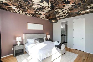 Ein Schlafzimmer mit einem großen Bett, zwei Nachttischen, einer Decke mit floralem Muster und einer Tür zu einem Badezimmer.