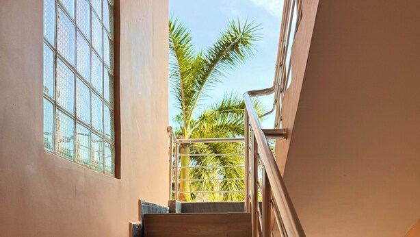 Una scala con gradini in legno e ringhiere in metallo, che conduce a un balcone con vista su palme.