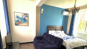 Una camera da letto con un letto, un divano, un quadro al muro e una finestra con tende.