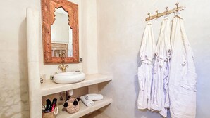 Un baño con lavamanos blanco, un espejo con marco de madera y un perchero con toallas blancas.