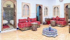 Un interior tradicional marroquí con un techo alto, puertas de madera ornamentadas y sofás rojos con estampado.