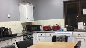 A kitchen with a wooden table, white cabinets, a microwave, and two red toasters. - THE RATHMORE (Cambridge)