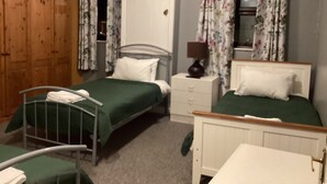 A bedroom with two beds, a wooden wardrobe, a bedside table with a lamp, and a mirror. - THE RATHMORE (Cambridge)