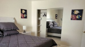 Ein Schlafzimmer mit Bett, Nachttisch, Deckenventilator und begehbarem Kleiderschrank.