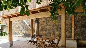 Una pérgola de madera al aire libre con una mesa y sillas, frente a un muro de piedra.