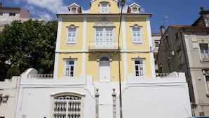 Un edificio amarillo con fachada blanca, un balcón y una entrada protegida por una reja.