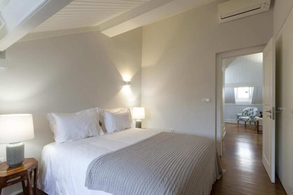 A bedroom with a bed, two bedside lamps, a nightstand, and a door leading to another room.