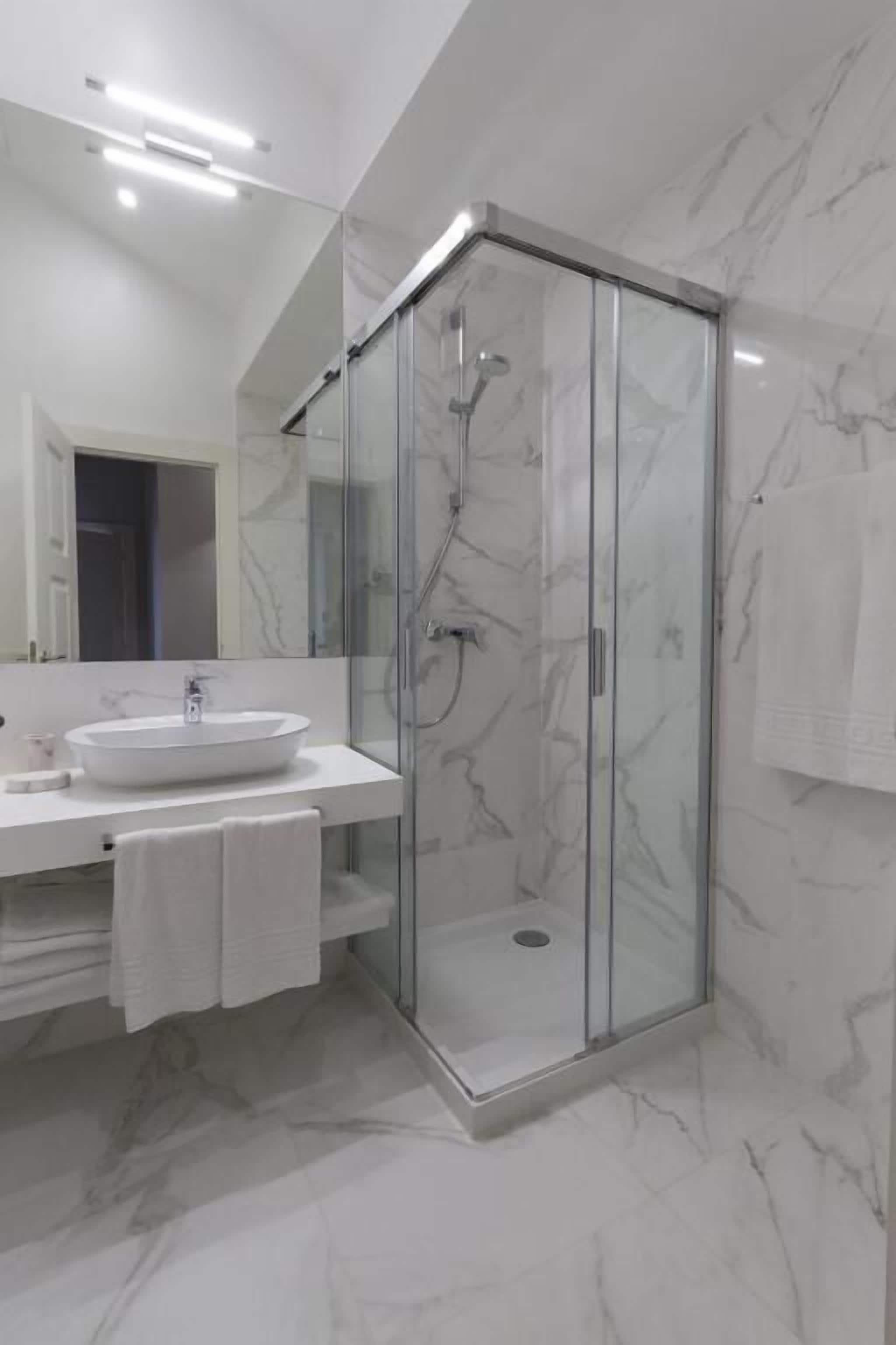 A modern bathroom with a glass-enclosed shower, a white sink, and marble walls.