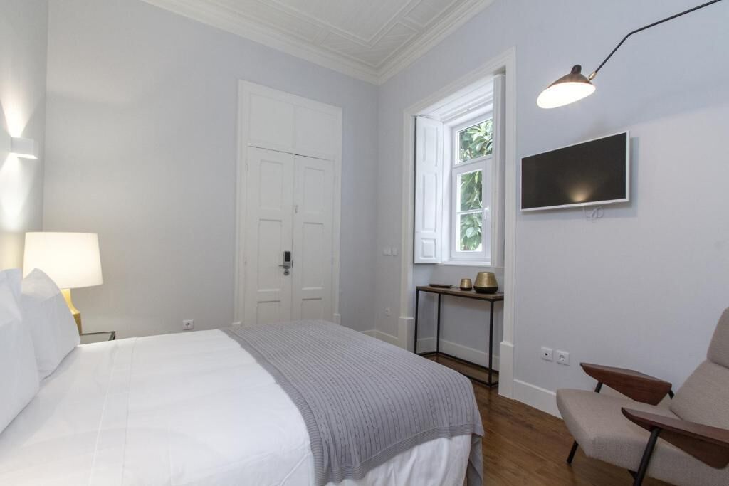 A hotel room with a bed, a desk, a chair, a TV, and a window with a view of greenery.