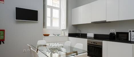 A modern kitchen with white cabinets, a glass dining table, and a black countertop.