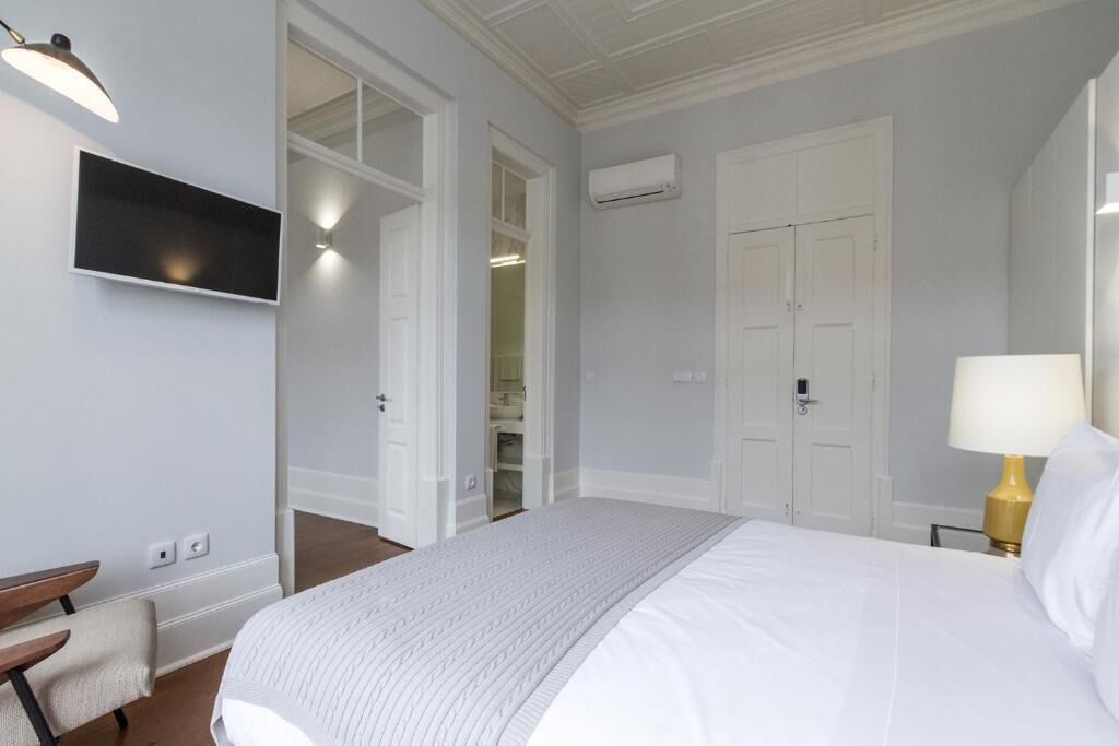 A hotel room with a bed, a desk, a chair, a TV, and a lamp.