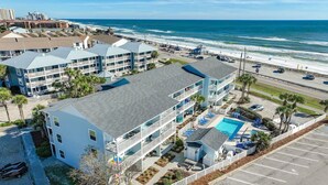 Ein Strandhotel mit mehreren Gebäuden, einem Swimmingpool und einem Parkplatz.
