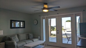 Ein Wohnzimmer mit einer Couch, einem Couchtisch, einem Deckenventilator, einer Uhr und einer Glastür, die nach draußen führt.