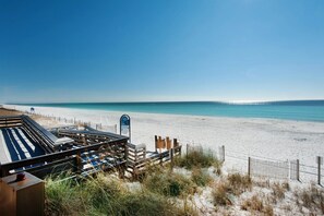 A beach with a wooden deck and lounge chairs, a sandy beach, and a clear blue sky. - Steps to the beach! 1-bedroom condo in charming Miramar Beach (Miramar Beach)