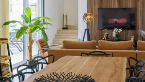 Una sala de estar moderna con una mesa de comedor de madera, sofás y un televisor de pantalla plana grande montado en una pared de madera.
