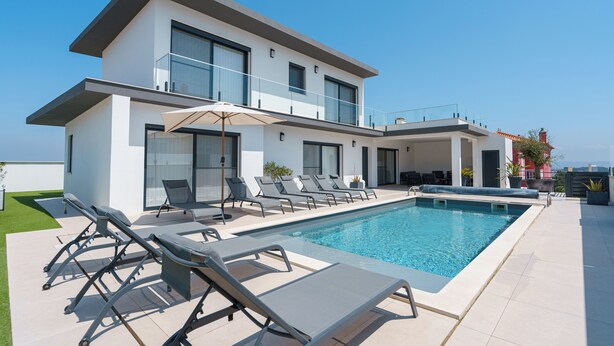 Una casa moderna de dos pisos con piscina, tumbonas y barandilla de cristal.