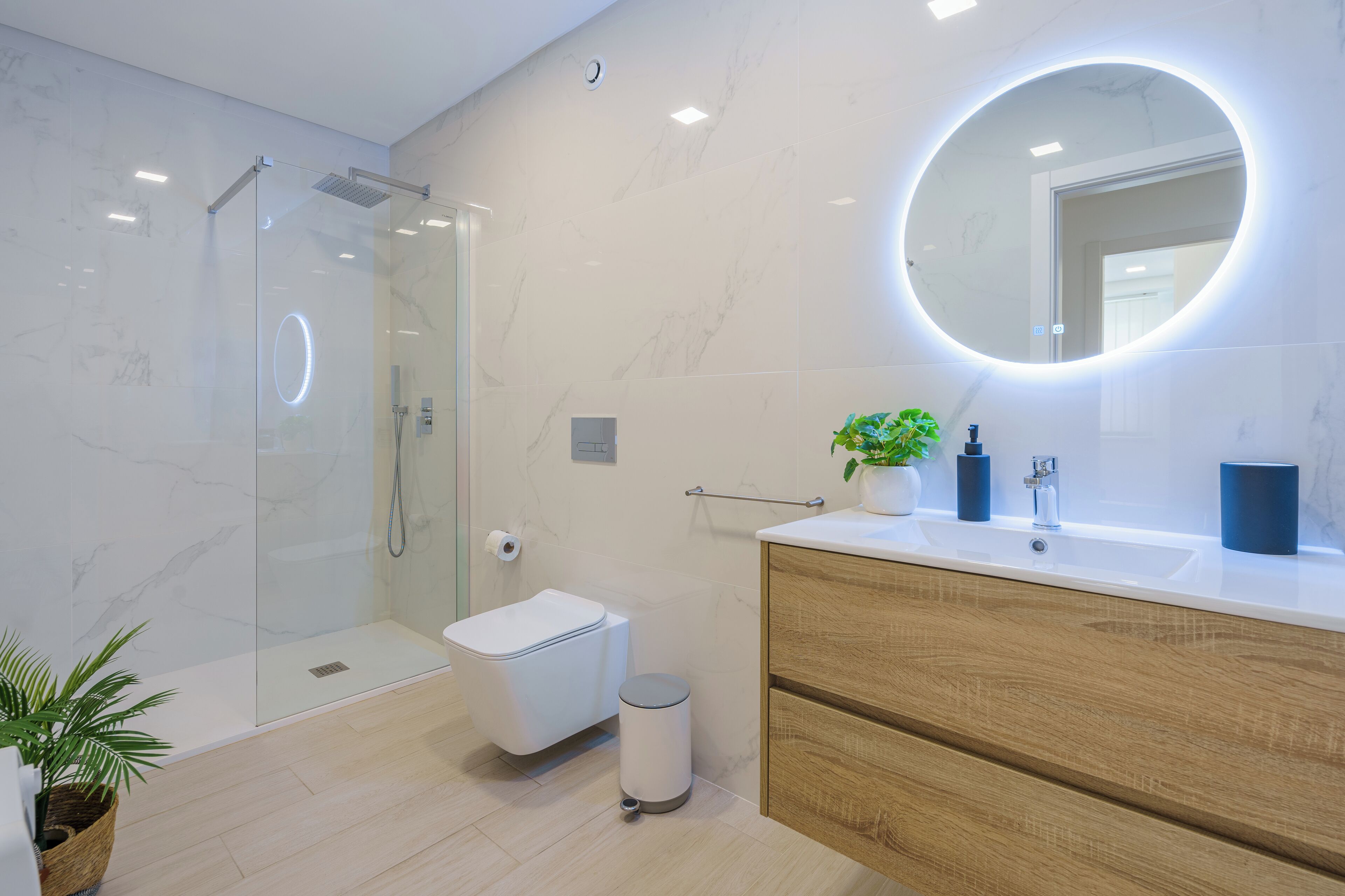 Een moderne badkamer met een douchecabine van glas, een toilet, een wastafel met spiegel en een houten wastafelmeubel.