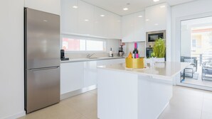 Una cocina moderna con armarios blancos, un refrigerador de acero inoxidable, una isla central y vistas al exterior.