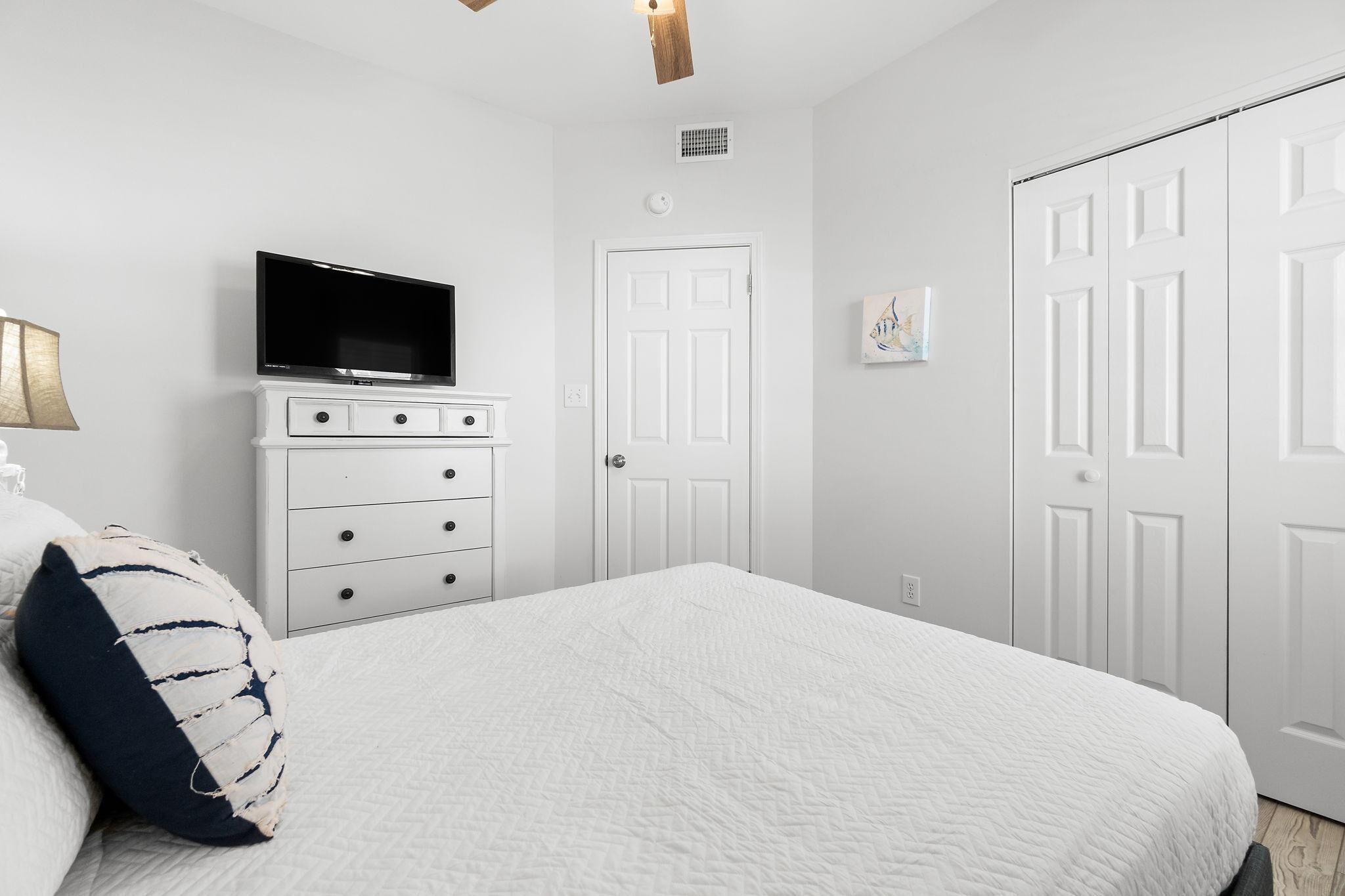 A bedroom with a bed, a dresser, a television, and white doors.