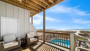 A wooden deck with a pool, wicker furniture, and a view of the beach.