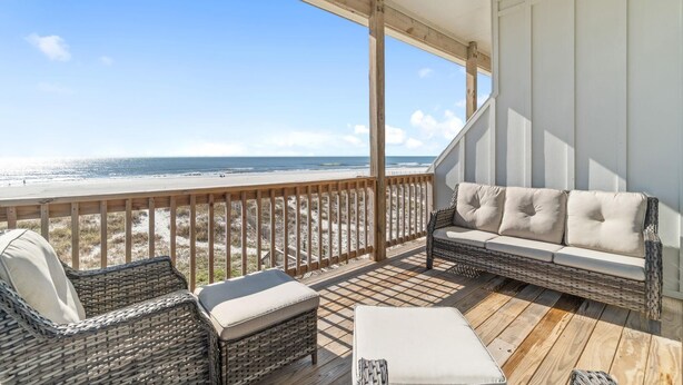 A wooden deck with wicker furniture and a sofa overlooking a beach.