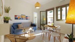 A modern living room with a blue sofa, a dining table with chairs, and a hanging light fixture. - Elartis Apartment (Chania)