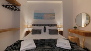 A bedroom with a bed, two bedside tables with lamps, a painting on the wall, a round mirror, and a wooden dresser. - Elartis Apartment (Chania)