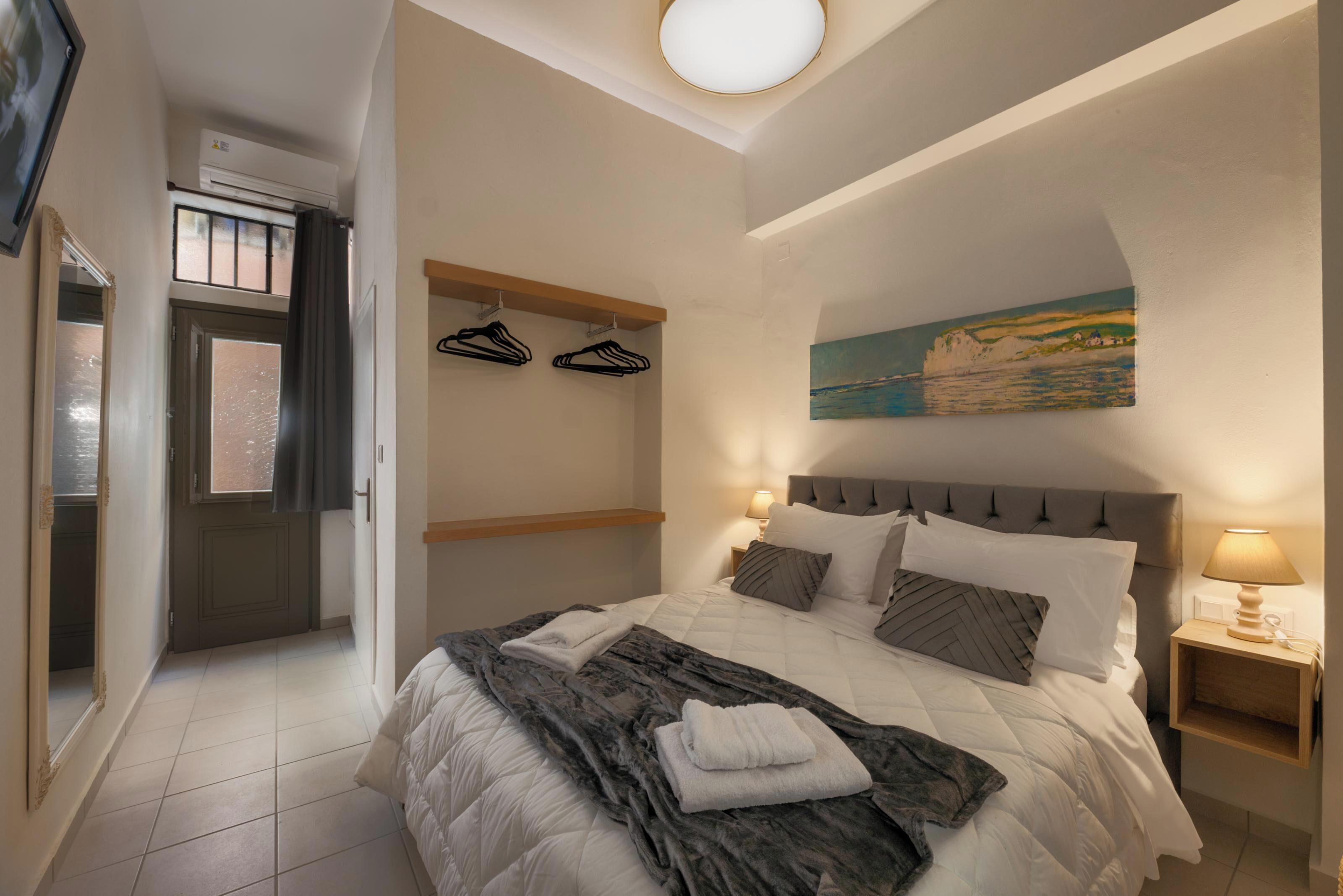 Une chambre à coucher avec un lit, une table de chevet, un tableau, une porte et un couloir.