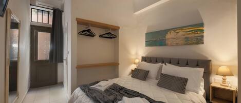 Une chambre à coucher avec un lit, une table de chevet, un tableau, une porte et un couloir.