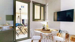A dining area with a round table, white chairs, and a TV mounted on the wall. - Elartis Apartment (Chania)