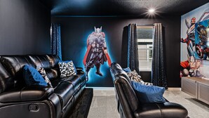 A room with a black leather couch, a black leather chair, and a wall mural of a superhero. - Amazing 6bed Home in Solara Fun for All (Kissimmee)