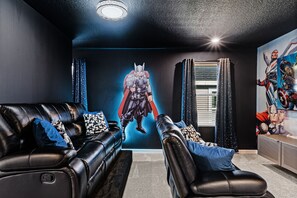 Una habitación con un sofá y una butaca de cuero negro, y un mural en la pared de un superhéroe.