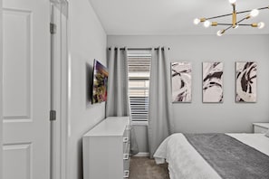 A bedroom with a bed, a dresser, a window with blinds, and three abstract paintings on the wall. - Amazing 6bed Home in Solara Fun for All (Kissimmee)