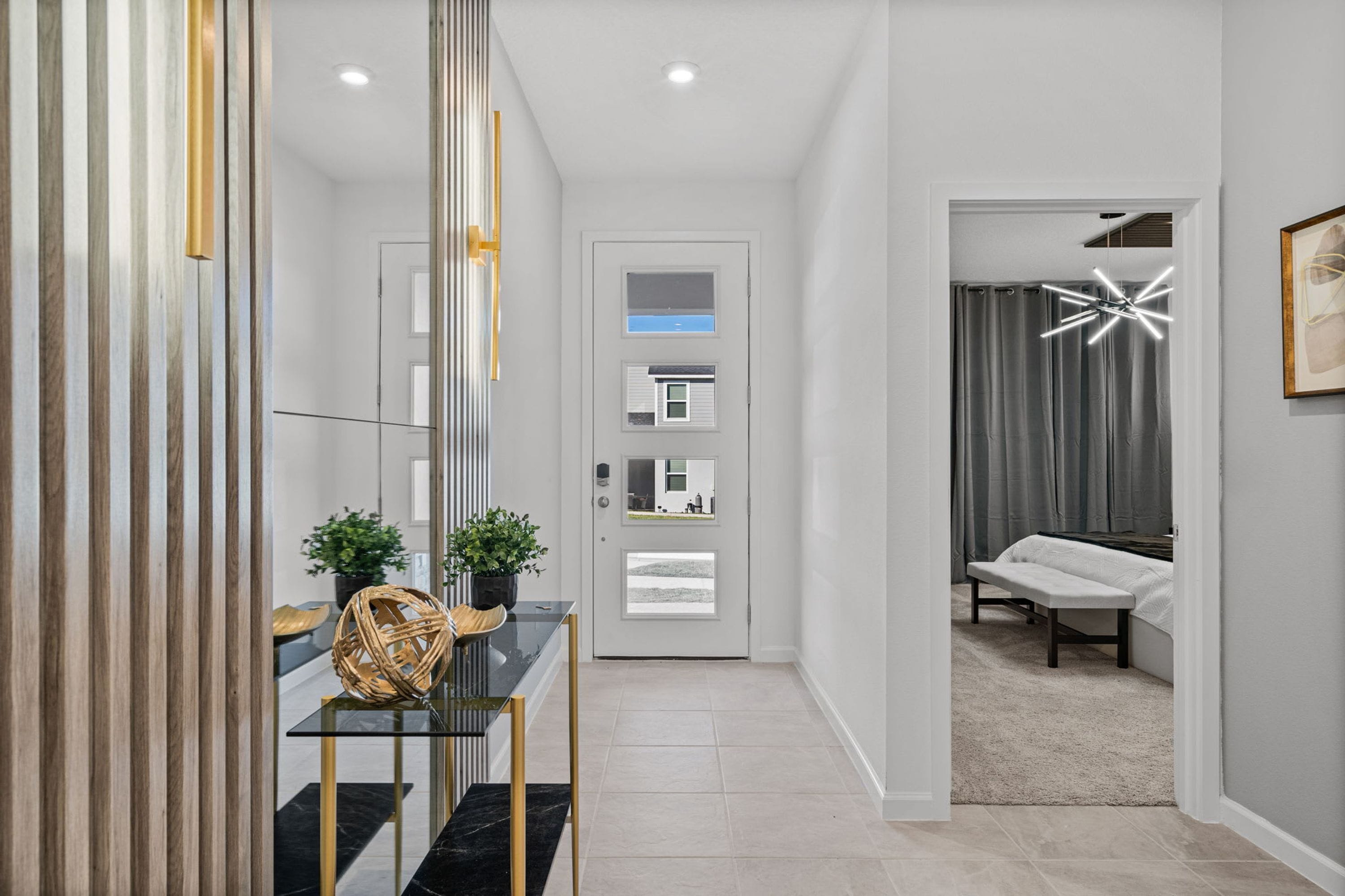 A modern hallway with a glass table, potted plants, and a bench.