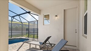 A sunlit patio with a swimming pool, two lounge chairs, and a door. - Amazing 6bed Home in Solara Fun for All (Kissimmee)