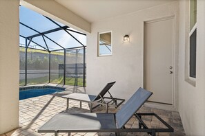 Un patio soleado con piscina, dos sillones de descanso y una puerta.