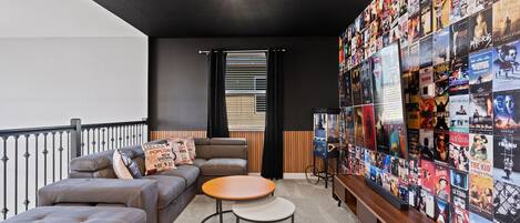A cozy living room with a sectional sofa, a round coffee table, and a wall adorned with movie posters.