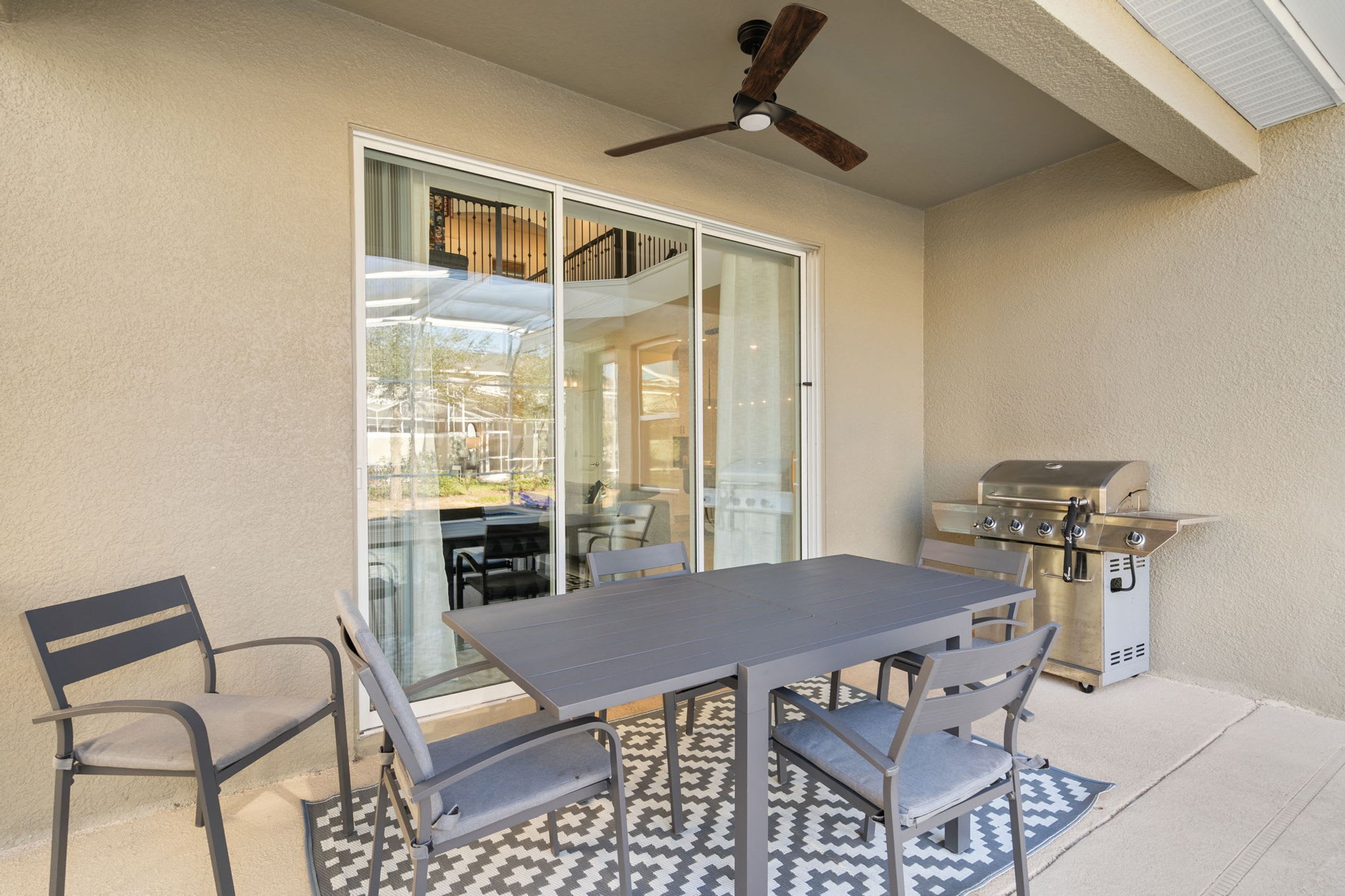 Patio esterno con tavolo e sedie, una ventola a soffitto e un barbecue.
