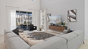 Uma sala de estar ampla com um sofá cinzento, uma mesa de centro e uma TV sobre um suporte de madeira.