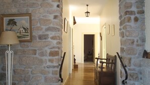 Un pasillo de paredes de piedra con un banco de madera, una lámpara y cuadros enmarcados.