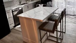 A modern kitchen with white cabinets, a marble island, and a dining area with a bench.