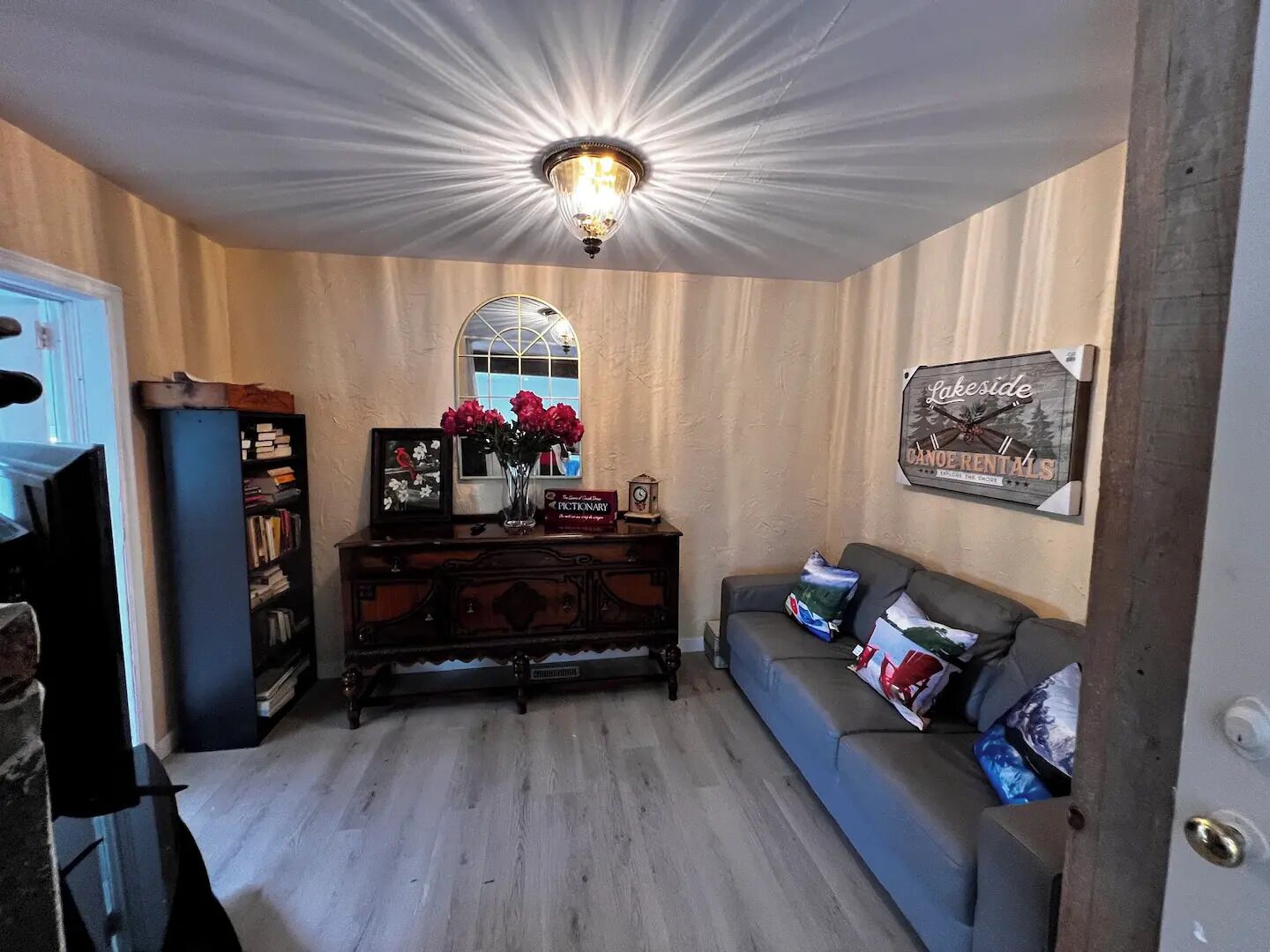 Ein gemütliches Wohnzimmer mit Holzboden, einem blauen Sofa, einem Holzschrank und einer dekorativen Deckenleuchte.