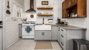 A kitchen with white wooden walls, a gas stove, a built-in oven, grey cabinets, and wooden shelves above the countertop.
