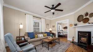A living room with a sofa, armchair, coffee table, fireplace, and ceiling fan.