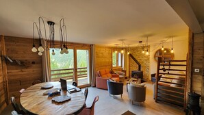 A cozy cabin interior with a wooden dining table, comfortable seating, a fireplace, and large windows offering a view of the forest. - 100% RENOVATED FAMILY CHALET with view! (Arvieux)