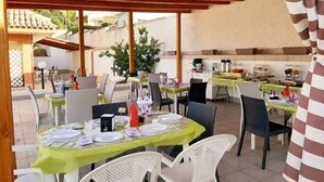 Un espace de restauration en plein air, avec des tables dressées pour les repas, abrité par une pergola en bois et entouré de chaises.